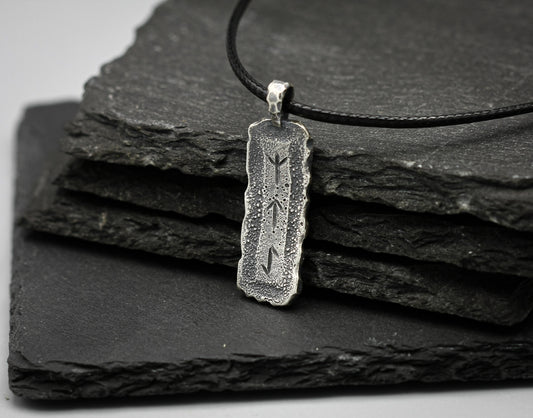 Silver pendant with engraved design on a black leather strap, placed on black slate stones.