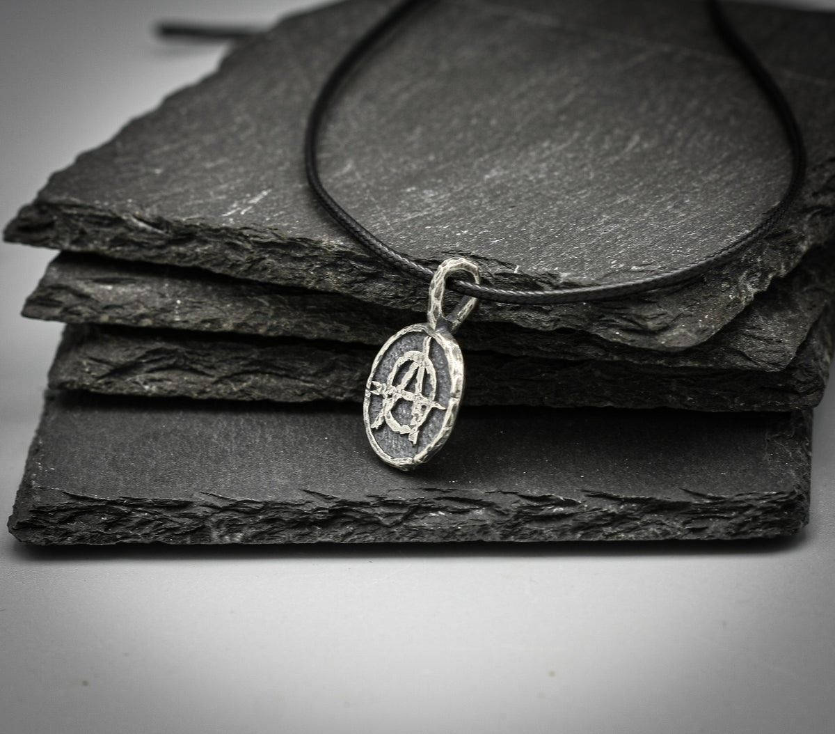 Angled view of sterling silver anarchy pendant showing textured edge and silver bail on a black cord