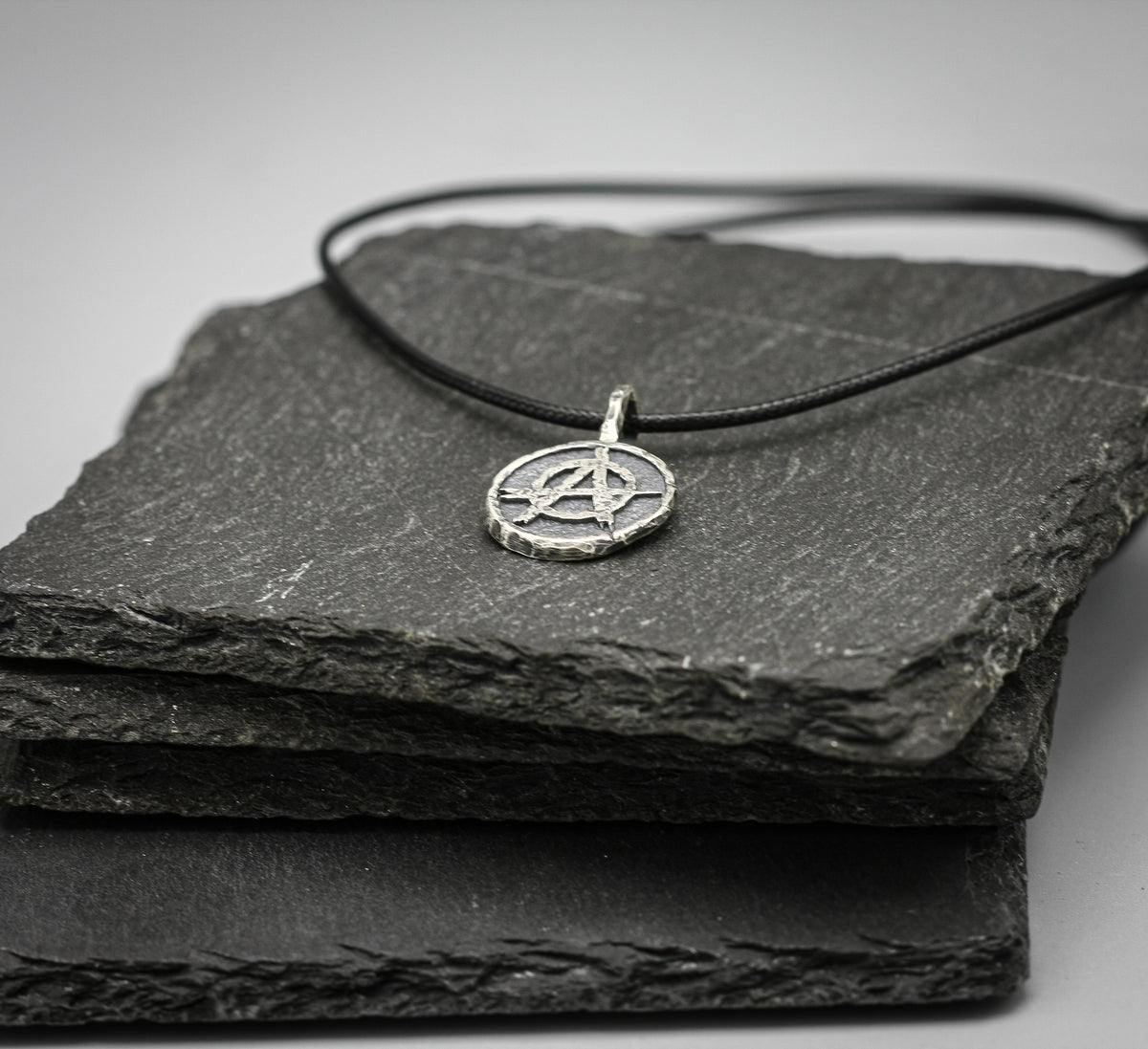 A silver pentagram pendant necklace on a black cord, displayed on stacked dark slate stones against a neutral gray background.