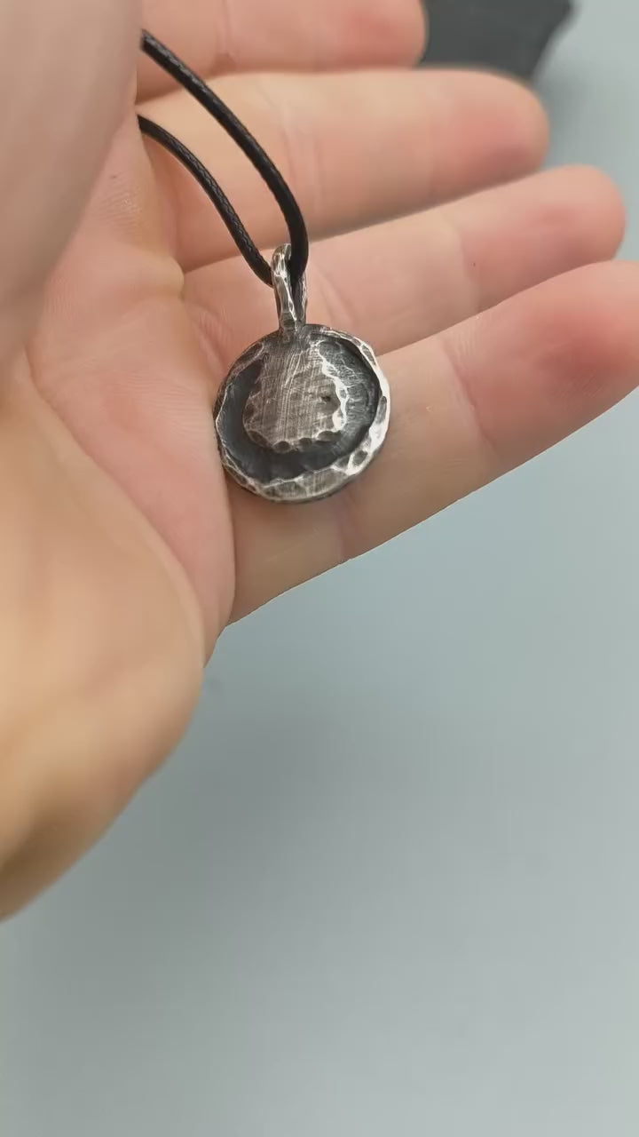 Sterling silver anarchy pendant lying flat on slate, showing raised symbol, textured finish and black cord